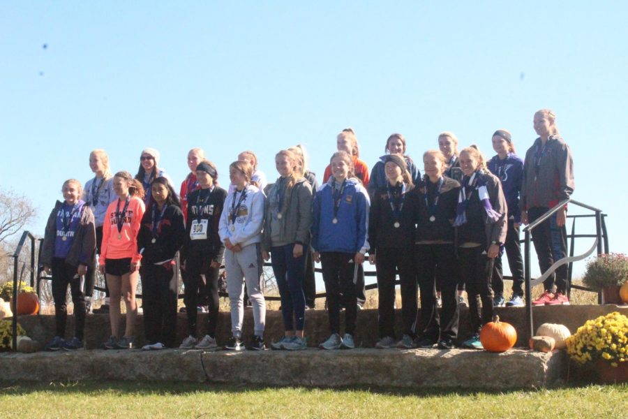 The Top 20 placers stand together a the awards ceremony. Jentrie Alderson places 1st wtih a time of 18:50.3--her time being 43.6 seconds faster than 2nd place-- and Ashley Prochazka places 10th with a time of 20:44.3.