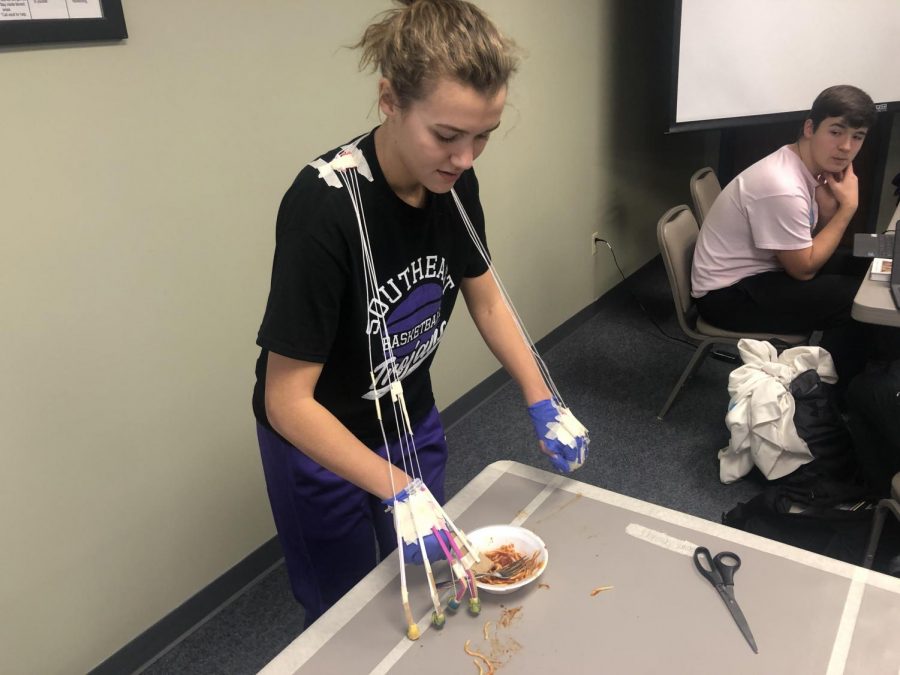 Madeline Blake tries to eat spaghetti with her prosthetic hand that she made in Anatomy and Physiology. The class did this project in the district office while they couldnt be in the classroom.